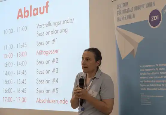Eine Frau steht mit einem Mikrofon vor einer Bühne.