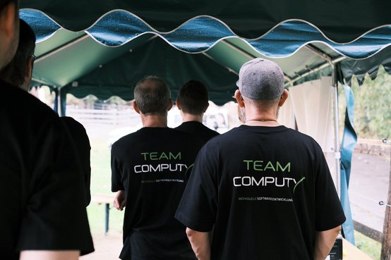 Das Computy-Team in Team-Shirts unter dem Zelt des Bogenschützenvereins, Blick auf die Wiese